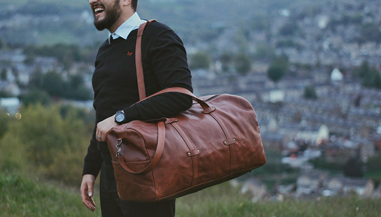 A man holding a Bayraw Travel Duffle standing on a hill in front of a cityscape